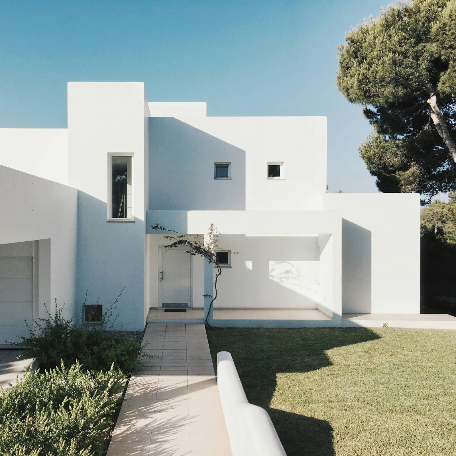 La villa vue depuis l'allée : des volumes blancs décalés, un pin parasol au-dessus